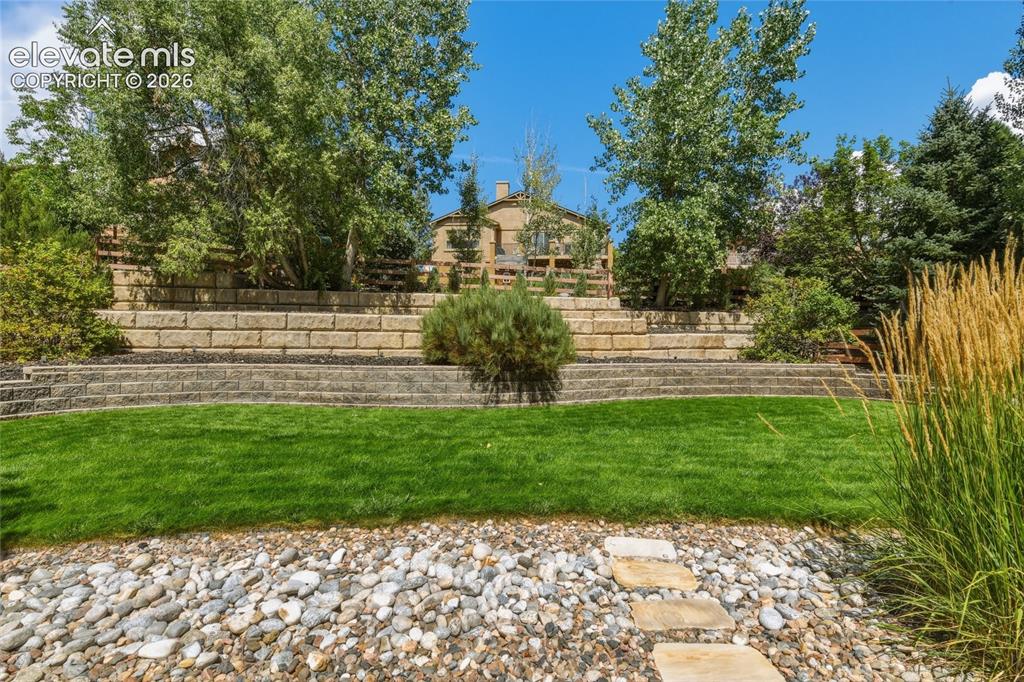 Image 39 of 49: Terraced landscaping with retaining walls, established trees, stone pathway