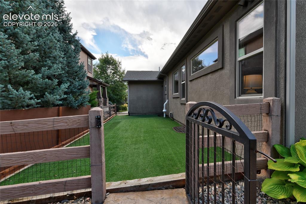 Image 41 of 49: Enclosed yard with artificial turf, a decorative wrought iron gate, and woo