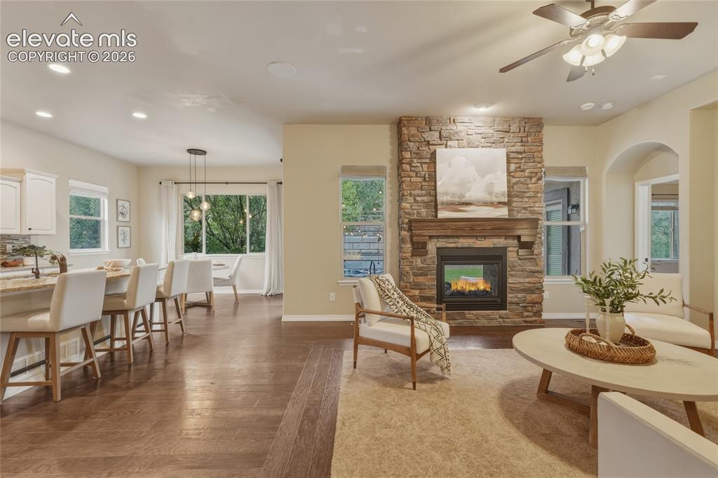Image 6 of 49: Stone-clad fireplace with a wood-finish mantel, ceiling fan, recessed light