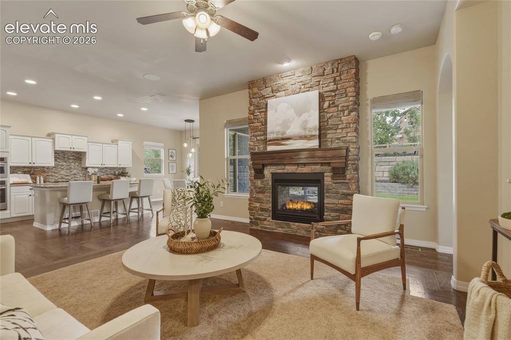 Image 8 of 49: Stacked stone fireplace with a substantial wood mantel, a ceiling fan with