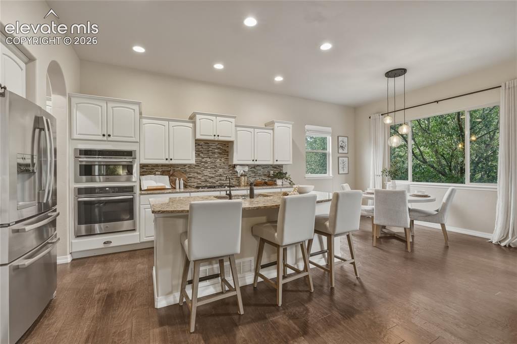 Image 9 of 49: Open-concept kitchen with wood-finish flooring, white cabinetry, stainless 