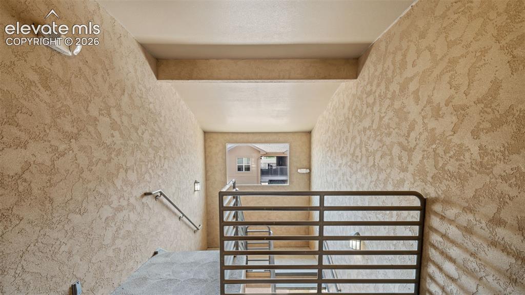Image 30 of 33: Stairwell with textured stucco walls, metal railings, and integrated wall s