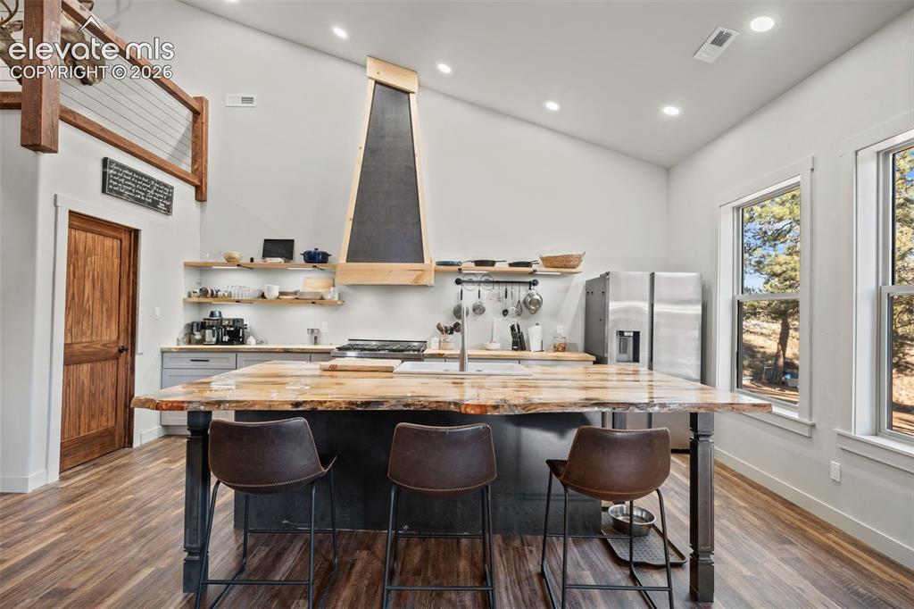 Image 13 of 42: Kitchen with vaulted ceiling, wood-finish flooring, two large windows, wood