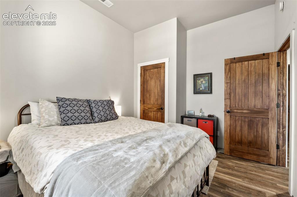 Image 27 of 42: Vaulted ceiling, wood-finish flooring, two natural wood doors with black ha