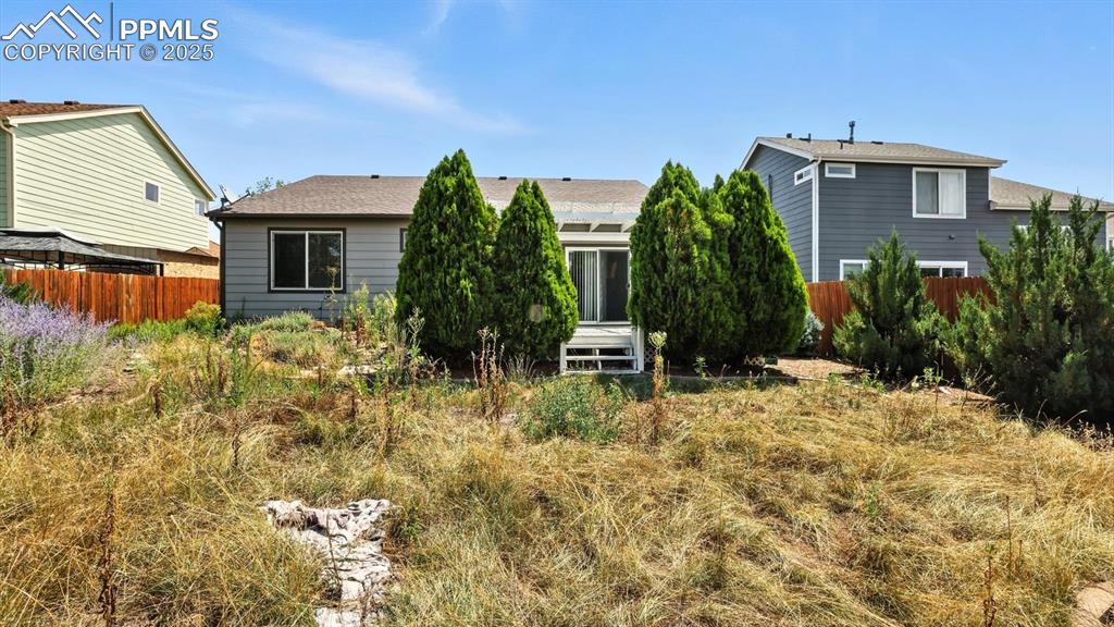Image 21 of 26: Rear view of home and fenced backyard with mature trees.