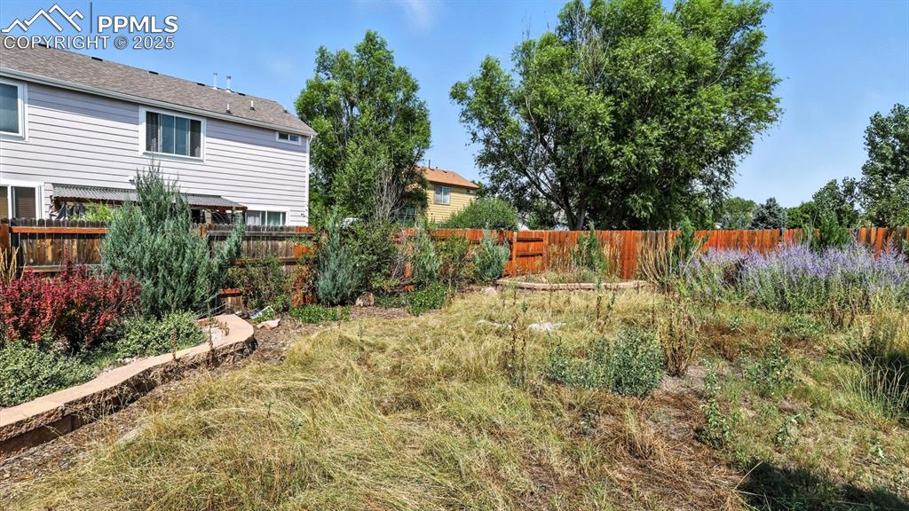 Image 22 of 26: Fenced backyard with mature trees, shrubs, and flower beds for the garden e