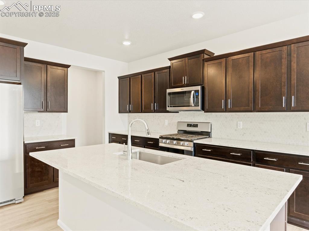 Image 10 of 32: Kitchen featuring dark brown cabinetry, appliances with stainless steel fin
