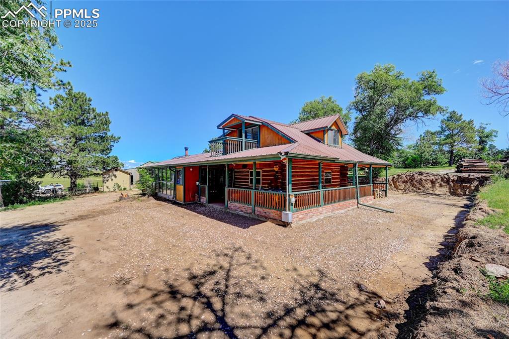 Image 6 of 50: View of front facade with log exterior, covered porch, metal roof, and driv