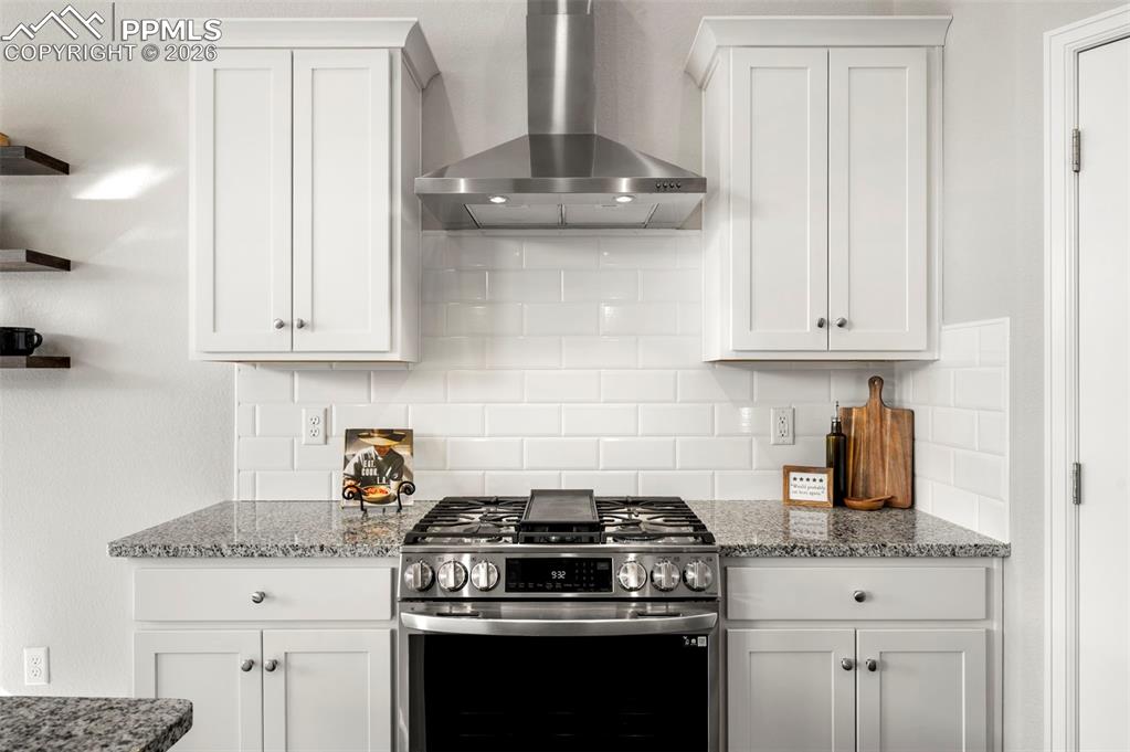 Image 19 of 49: Kitchen with stainless steel gas stove, white cabinetry, light stone counte