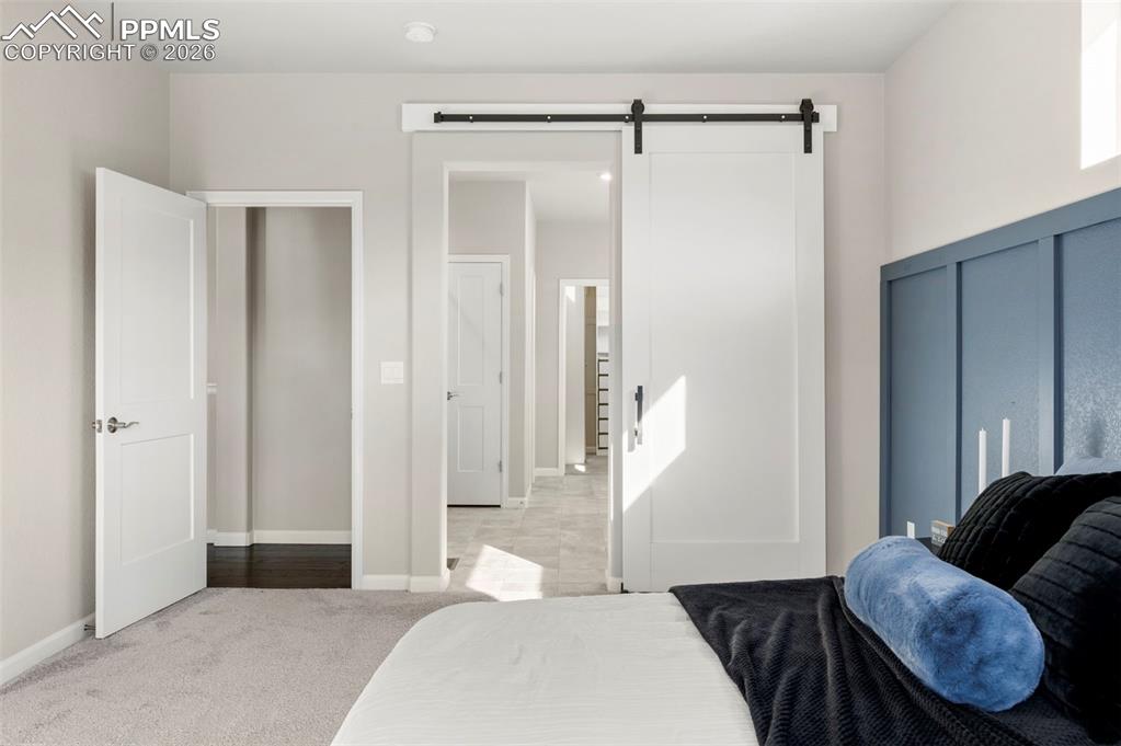 Image 24 of 49: Bedroom with a barn door, light colored carpet, and a decorative wall