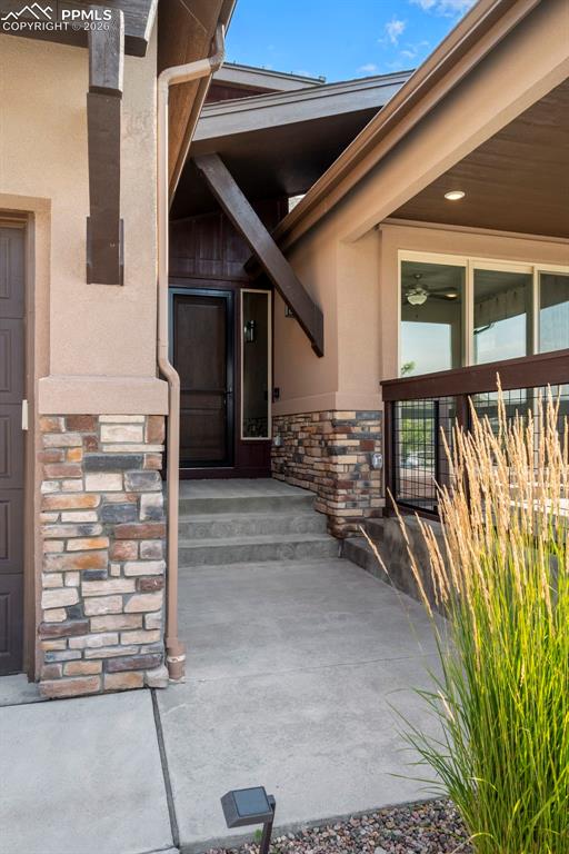 Image 7 of 49: View of exterior entry featuring stone siding, stucco siding, and a patio