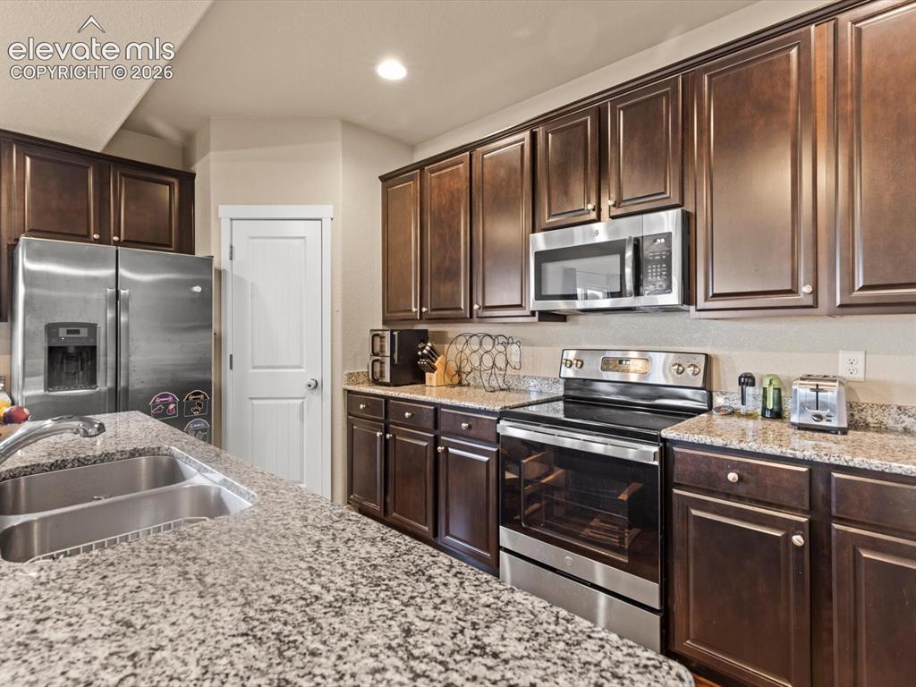 Image 19 of 45: Kitchen featuring extensive granite countertops, dark wood cabinetry, stain