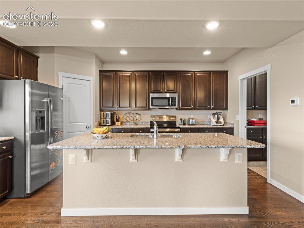 Image 21 of 45: Central kitchen island with a speckled countertop, dark wood-finish cabinet