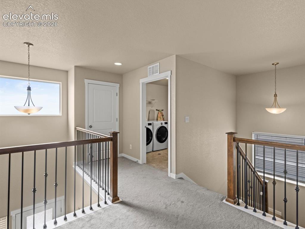 Image 24 of 45: Upper-level landing featuring neutral carpeting, a white paneled door, and 