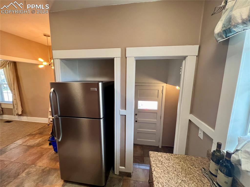 Image 17 of 18: Kitchen with stainless steel refrigerator, an inviting chandelier, dark til
