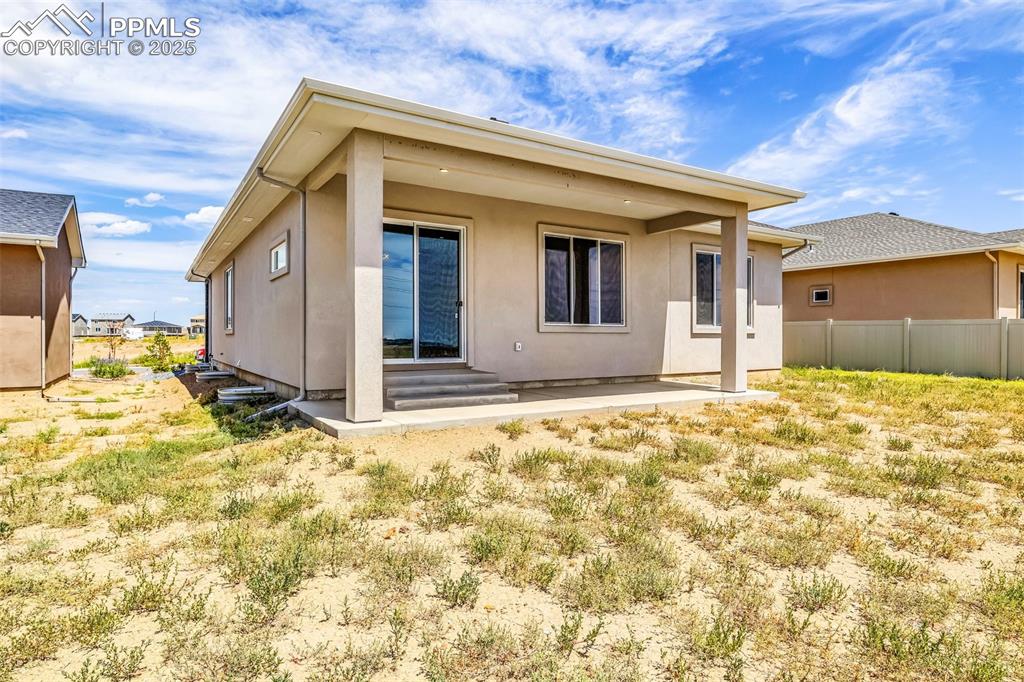 Image 13 of 50: Back of house featuring entry steps, fence, and stucco siding