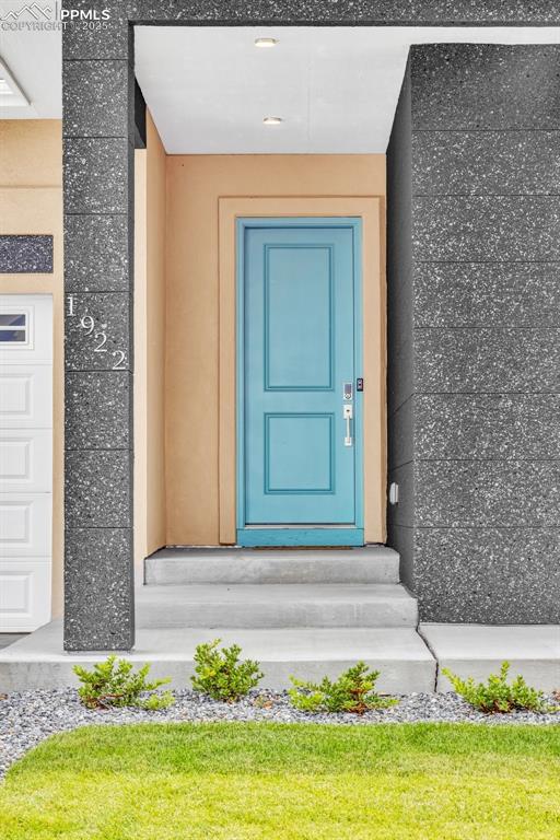 Image 3 of 50: Doorway to property with stucco siding and a garage