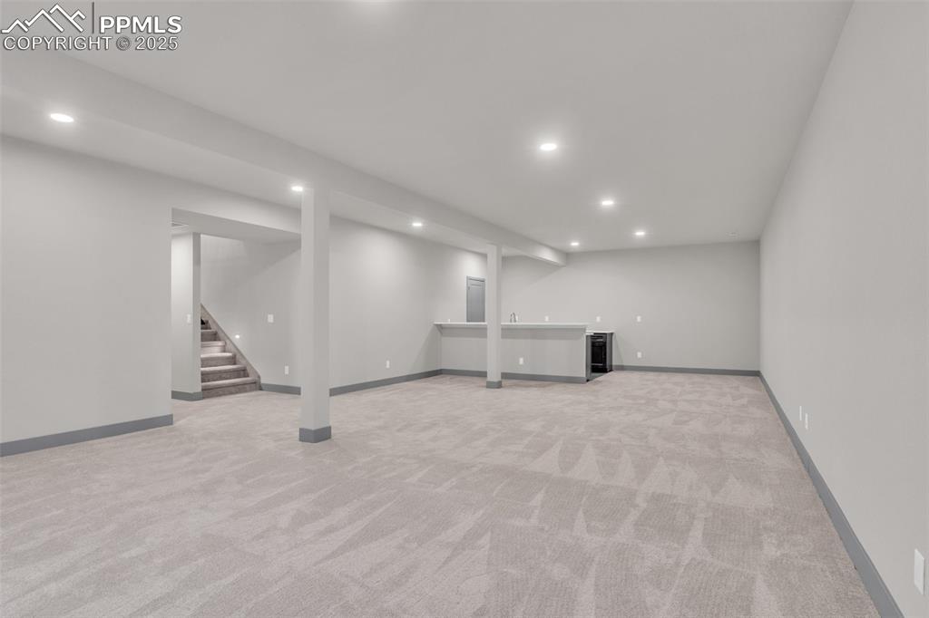 Image 35 of 50: Finished below grade area with wet bar, stairway, recessed lighting, and li