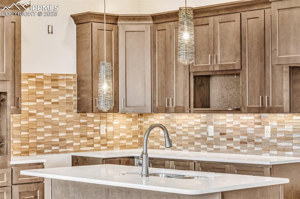Image 49 of 50: Kitchen featuring hanging light fixtures, light countertops, tasteful backs