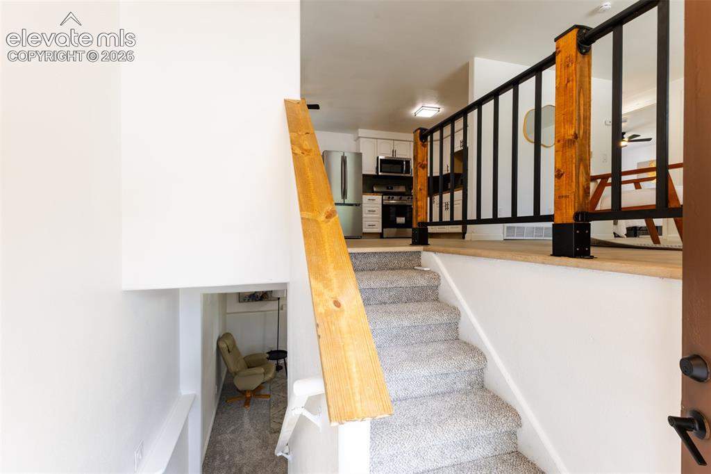 Image 12 of 32: Carpeted staircase with a wood handrail, leading to a landing with a black 