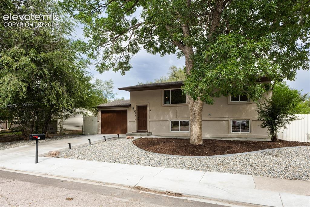 Image 2 of 32: Stucco exterior, attached garage with wood-finish door, concrete driveway, 
