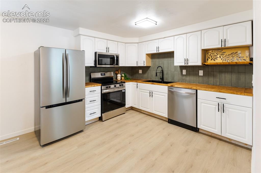 Image 6 of 32: Kitchen featuring stainless steel appliances, white cabinetry, wood-finish 