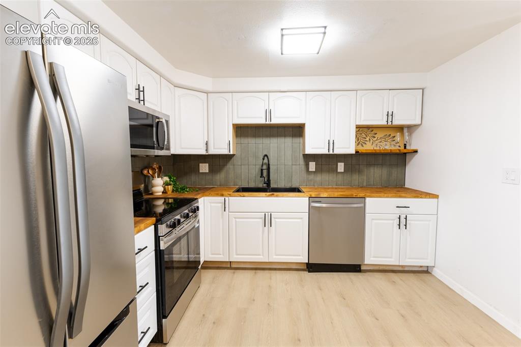 Image 7 of 32: Kitchen featuring white cabinetry, wood-finish countertops, stainless steel