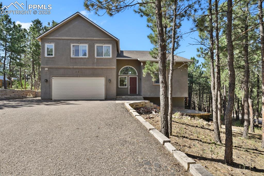 Caption: View of front of property with gravel driveway, stucco siding, a garage, and roof with shingles