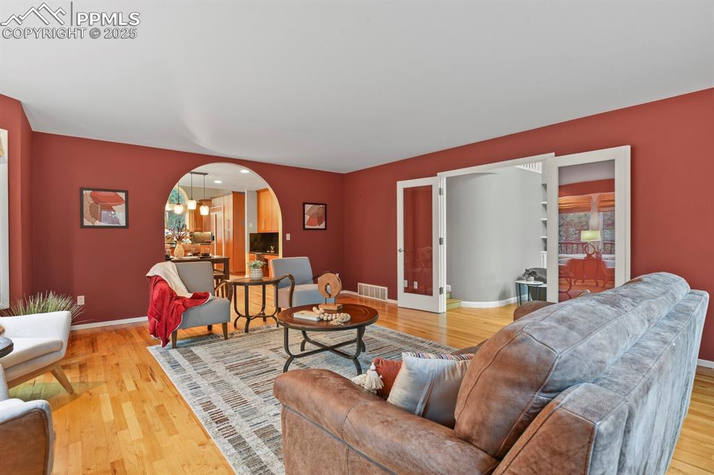 Image 14 of 50: Living room with arched walkways, light wood finished floors, and french do