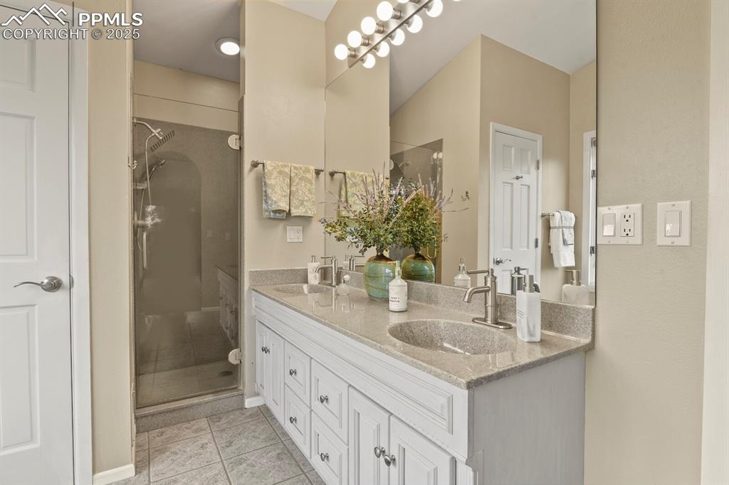 Image 25 of 50: Full bathroom with double vanity, a shower stall, and tile patterned floors
