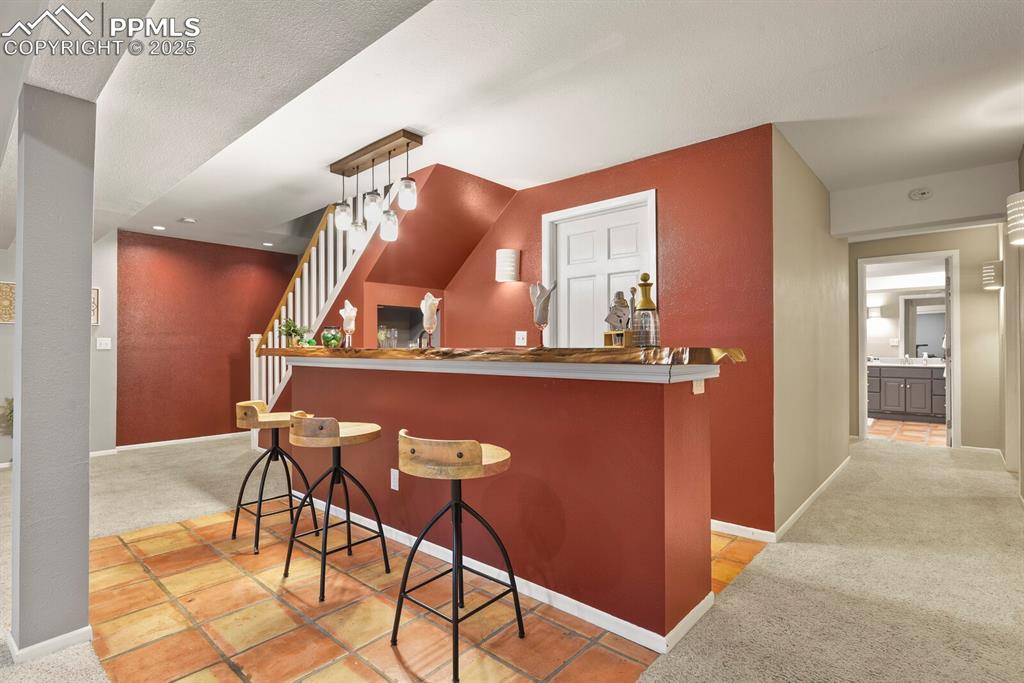 Image 34 of 50: Bar area with carpet, stairway, and tile patterned flooring
