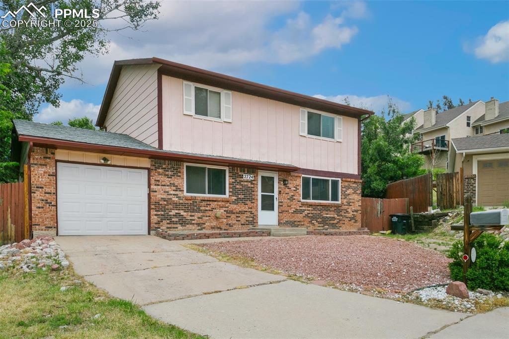 Caption: View of front of house with brick siding, driveway, and a garage