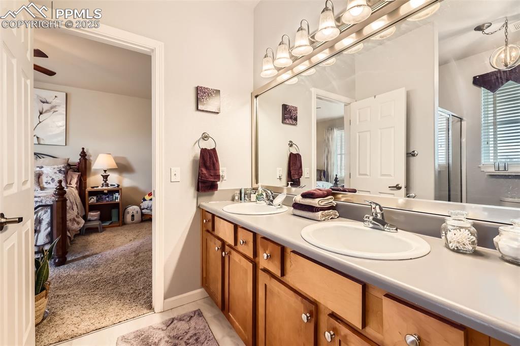 Image 16 of 26: Ensuite bathroom featuring double vanity, a shower with door, and tile patt