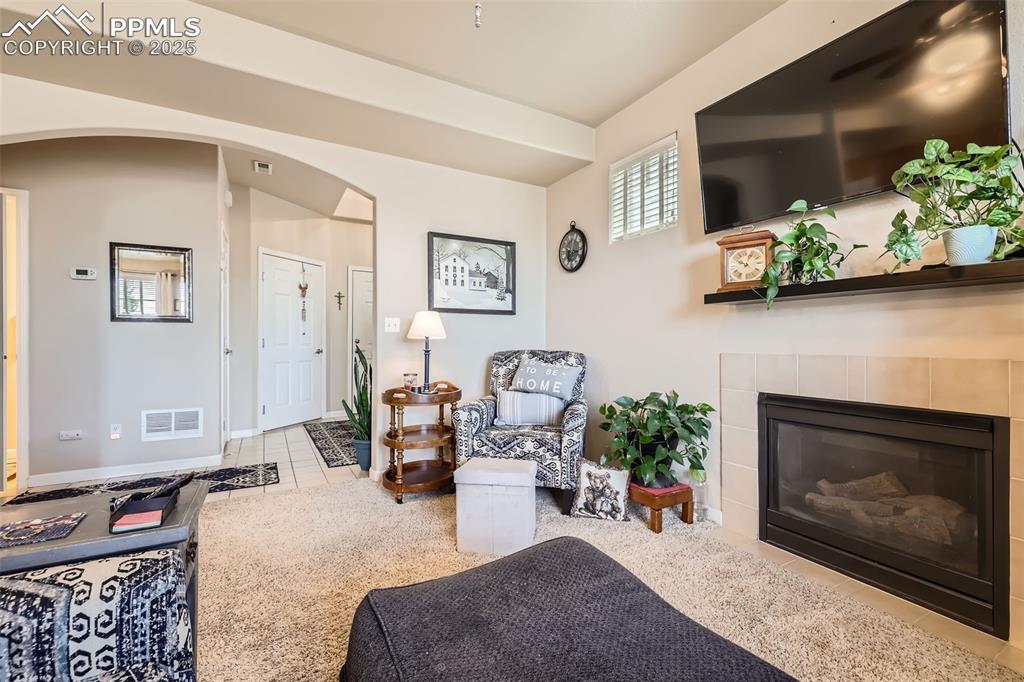 Image 6 of 26: Tiled living area with arched walkways, a tiled fireplace, and carpet