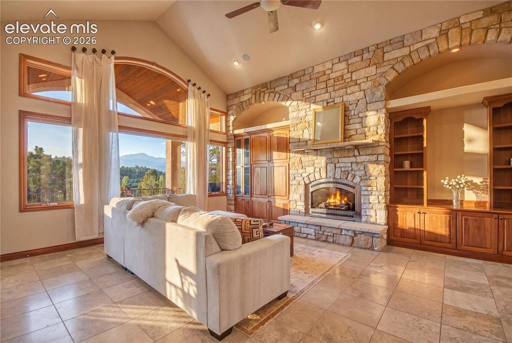 Image 11 of 50: Spacious living area featuring a stone-clad fireplace with a hearth, arched