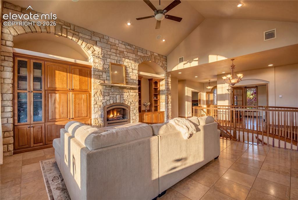 Image 12 of 50: Spacious living area featuring a vaulted ceiling, stone fireplace, built-in