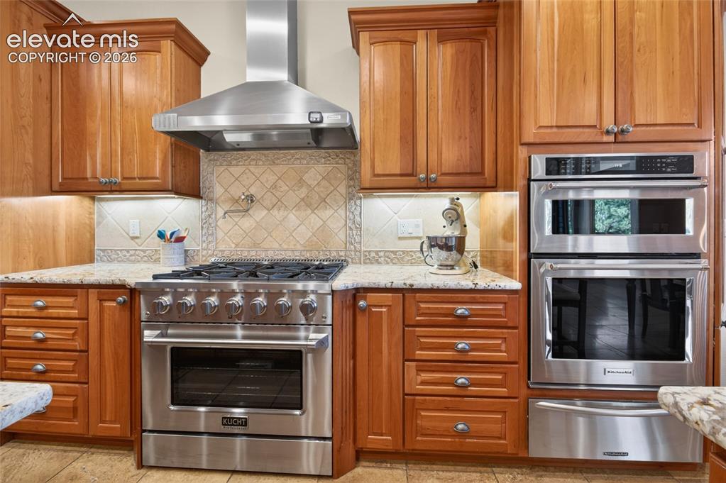 Image 17 of 50: Kitchen featuring wood cabinetry, stainless steel appliances, granite count