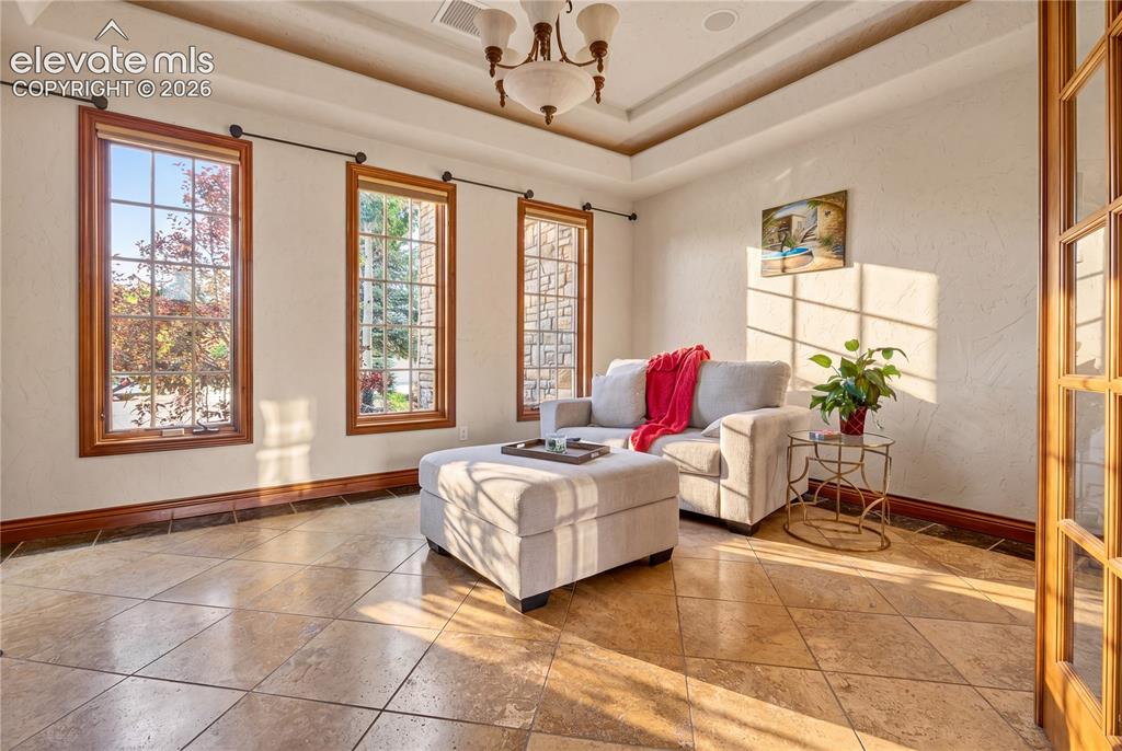 Image 19 of 50: Room featuring large windows with wood trim, tray ceiling with chandelier,