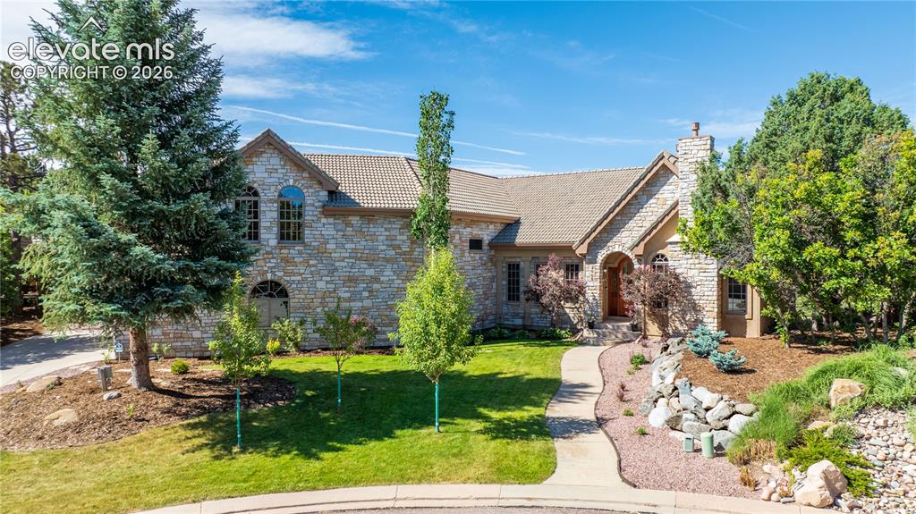 Image 2 of 50: Stone facade residence featuring a tiled roof and prominent chimney