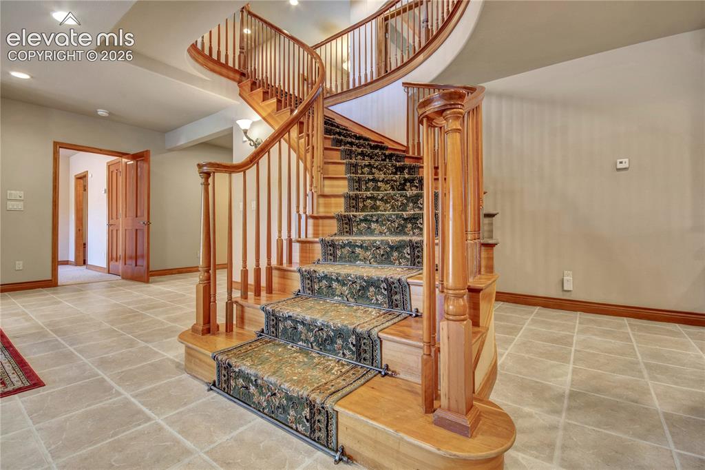 Image 34 of 50: Grand curved staircase featuring wood treads and banisters, wrought iron ne