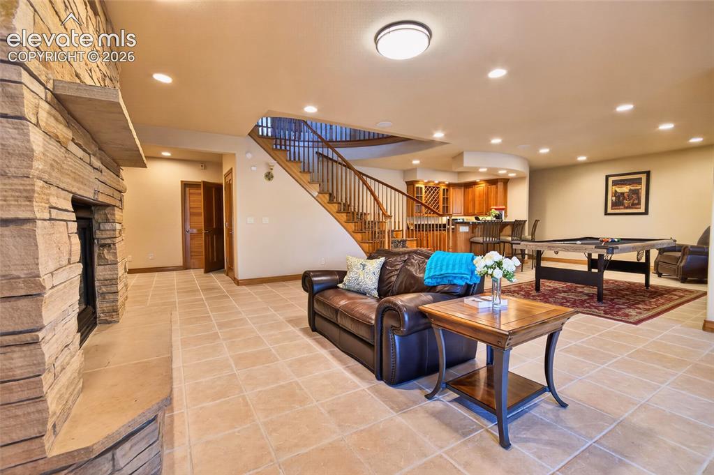 Image 37 of 50: Spacious lower level featuring a stone-clad fireplace, tile flooring, built