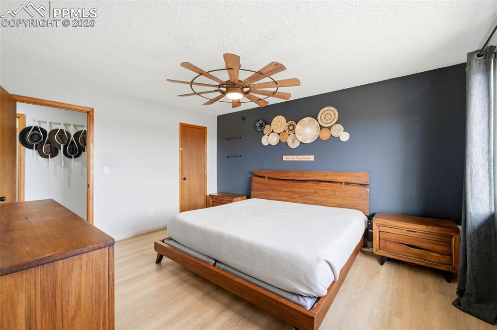 Image 19 of 37: Bedroom with light wood finished floors, ceiling fan, and a textured ceilin