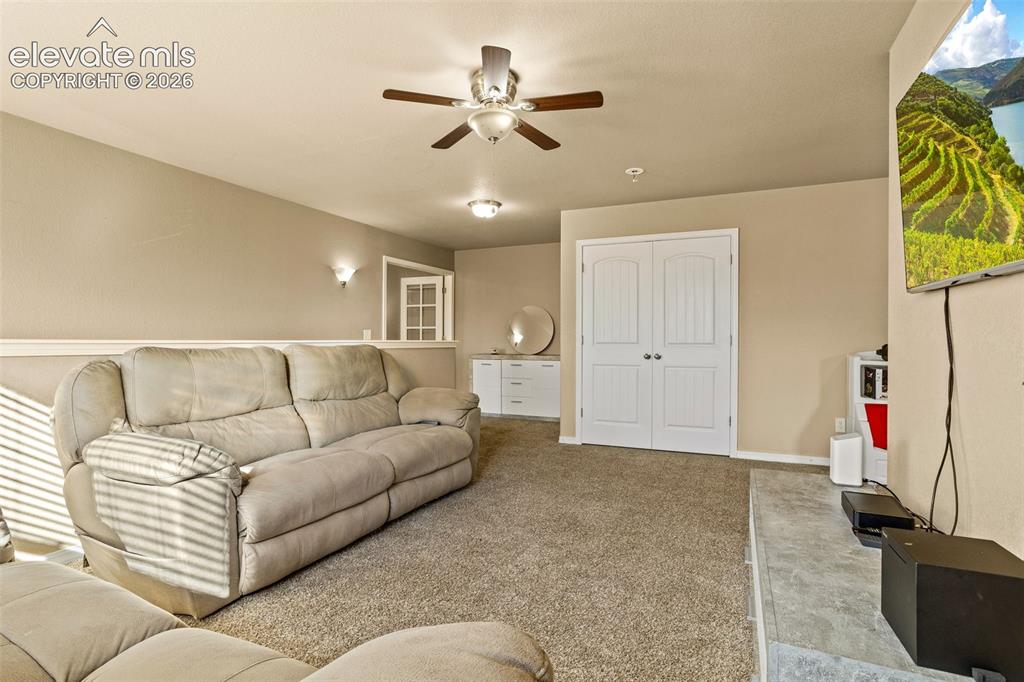 Image 11 of 30: Carpeted recreation room featuring a ceiling fan, dual wall sconces, and bu