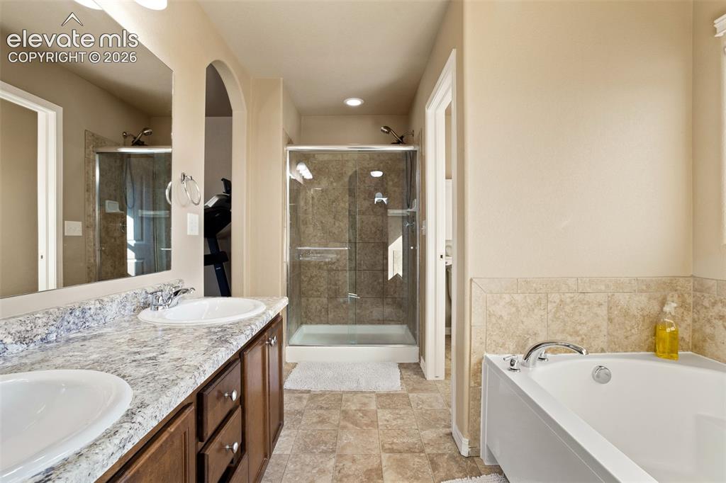 Image 15 of 30: Dual vanity with integrated sinks, a glass-enclosed shower with tiled surro