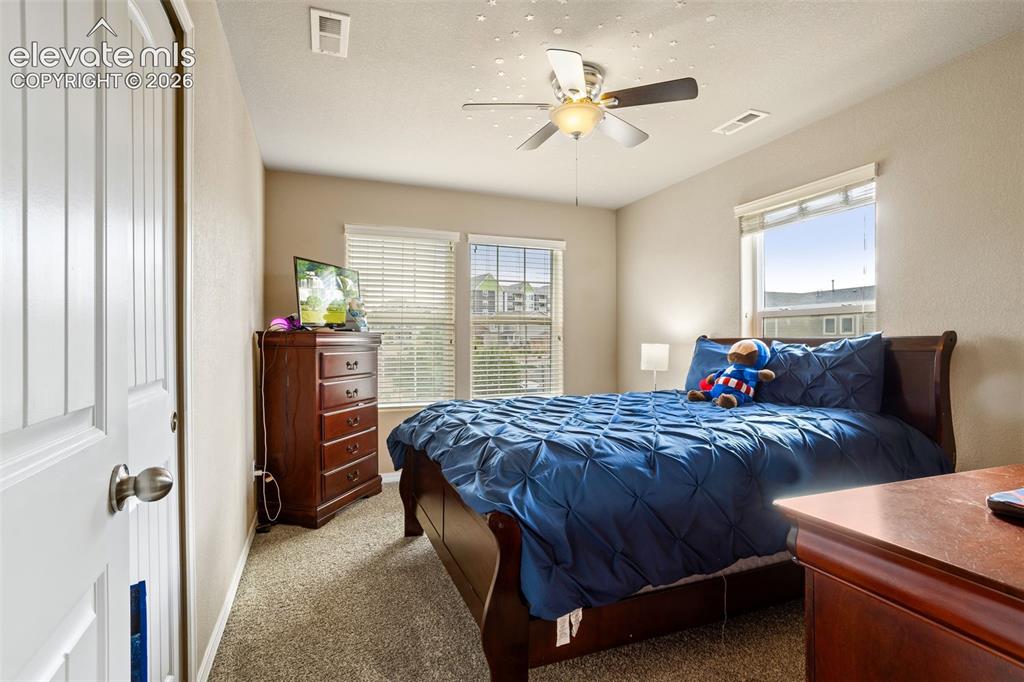 Image 18 of 30: Ceiling fan with integrated lighting, two windows with blinds, carpeted flo
