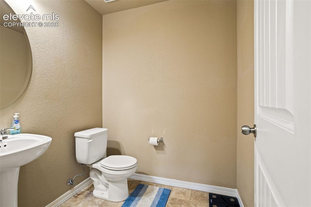 Image 20 of 30: Pedestal sink with an oval mirror, white toilet, and sheet vinyl flooring