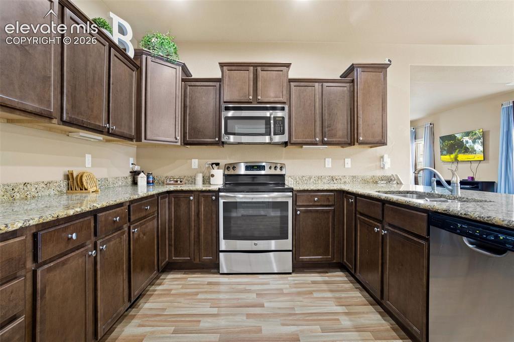 Image 7 of 30: Kitchen featuring wood-finish flooring, dark wood cabinetry, light-toned co