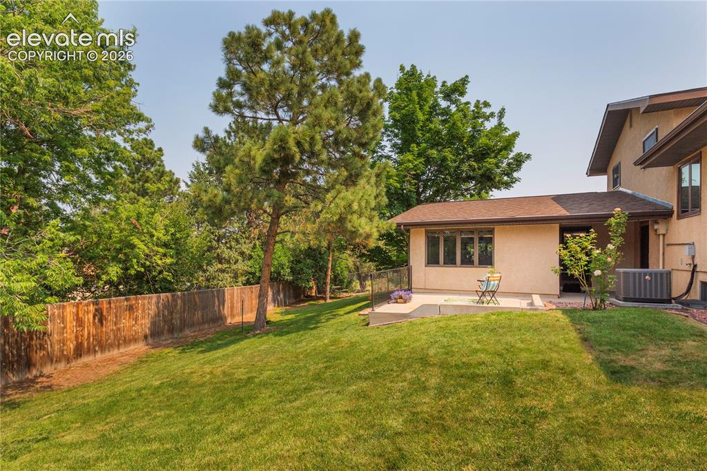 Image 19 of 50: Expansive sloped lawn with mature trees and a wood privacy fence.