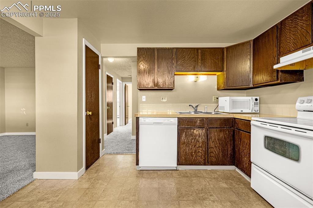 Image 8 of 15: Kitchen with white appliances, dark brown cabinets, a textured ceiling, und