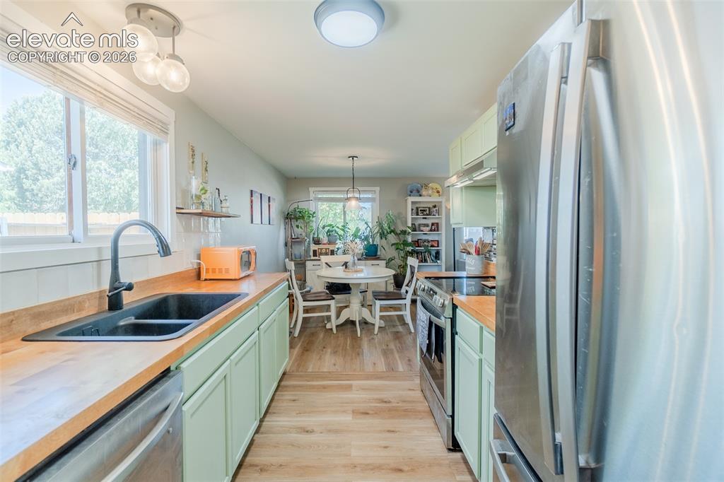 Image 12 of 31: Kitchen featuring light green cabinetry, wood-finish countertops, and stain